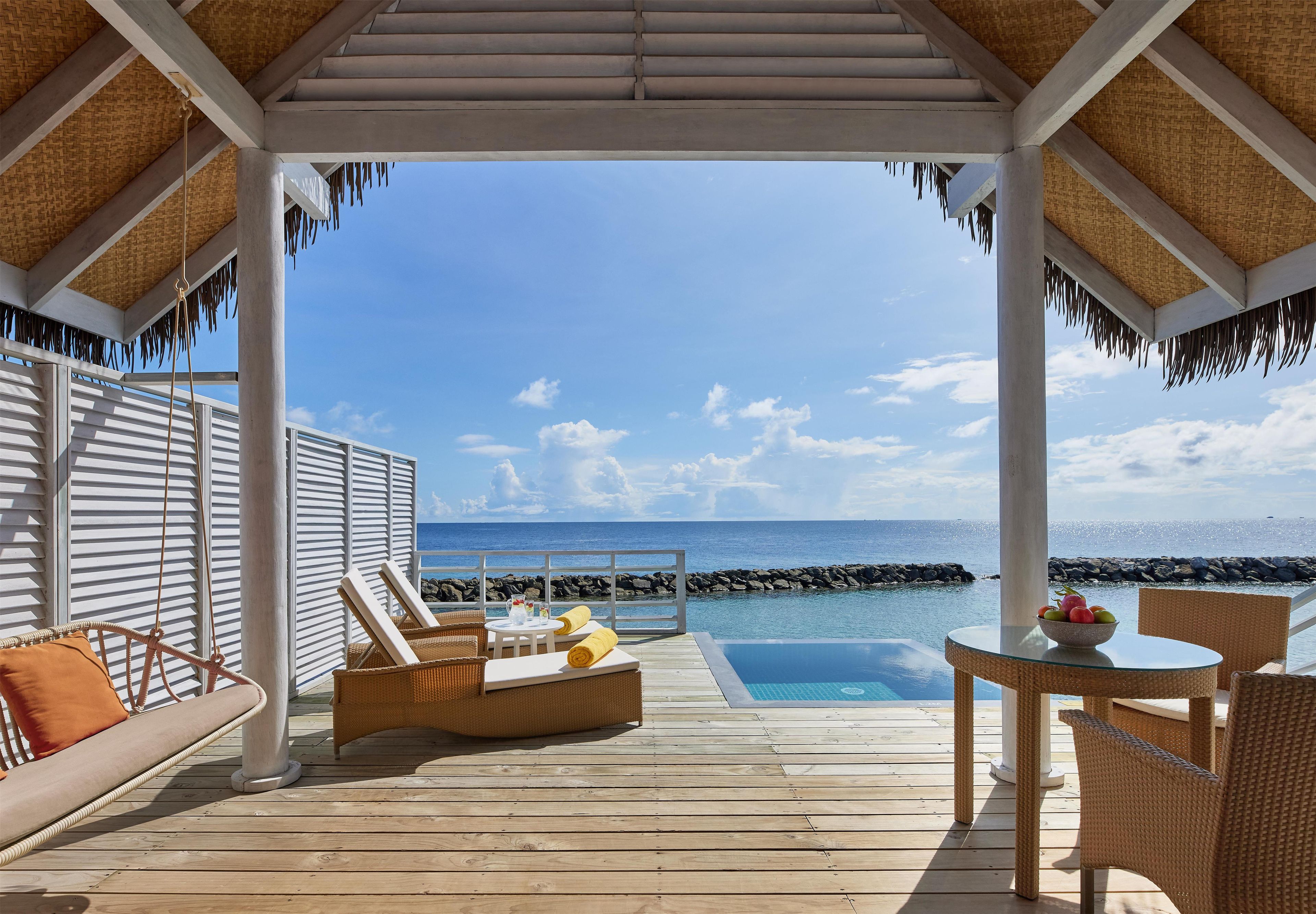 A wooden deck with a pool, lounge chairs, and a table with fruit.