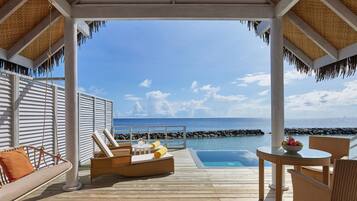 A wooden deck with a pool, lounge chairs, and a table with fruit.