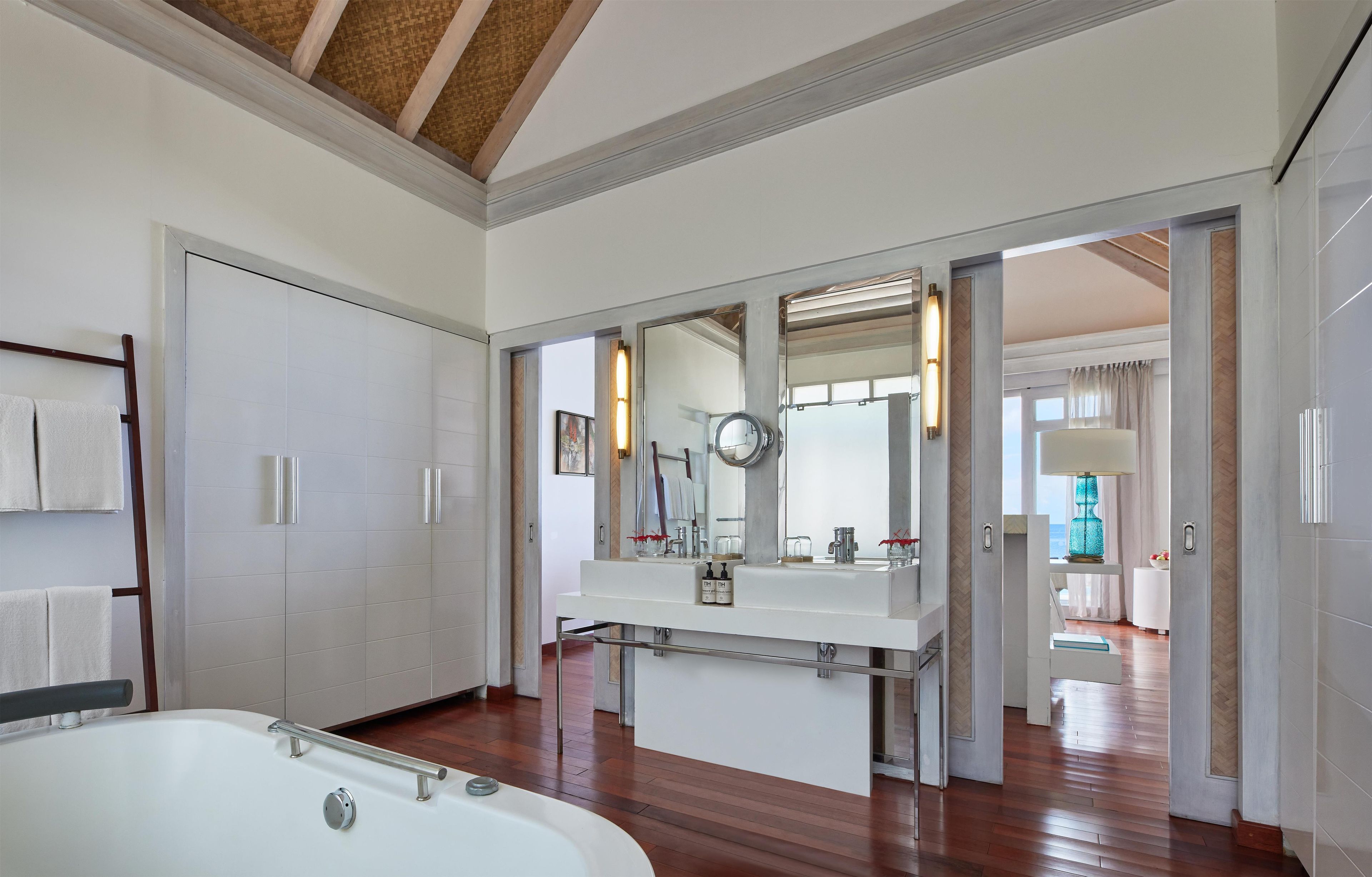 A modern bathroom with a large bathtub, a vanity with a mirror, and a view of the adjacent room.