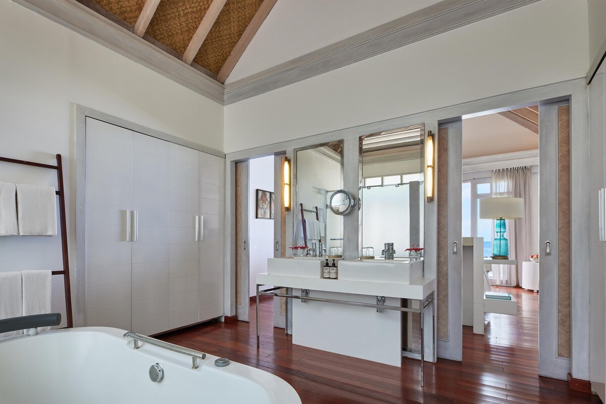 A modern bathroom with a large bathtub, a vanity with a mirror, and a view of the adjacent room.