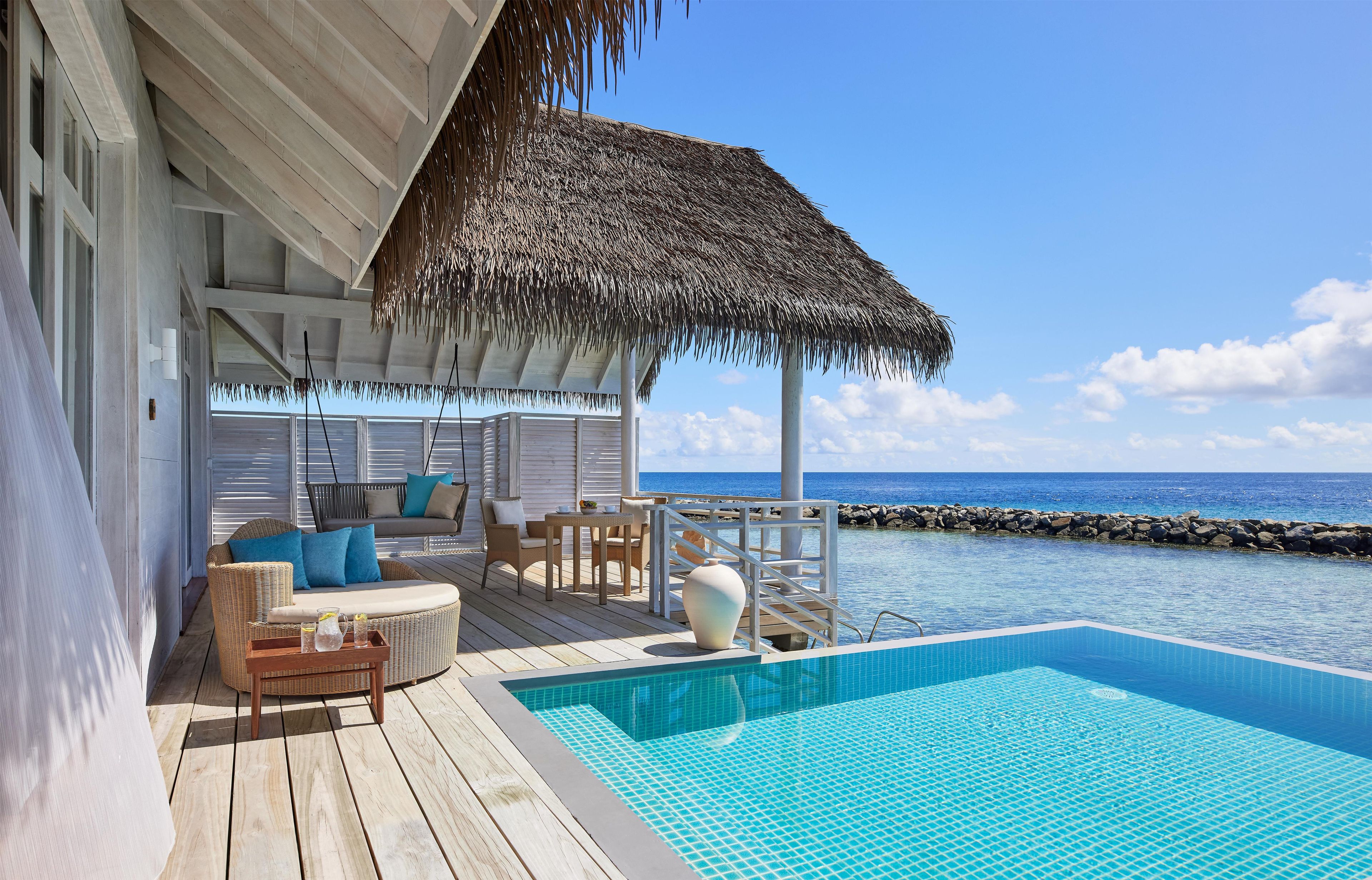 A poolside area with a thatched roof, wicker furniture, and a view of the ocean.