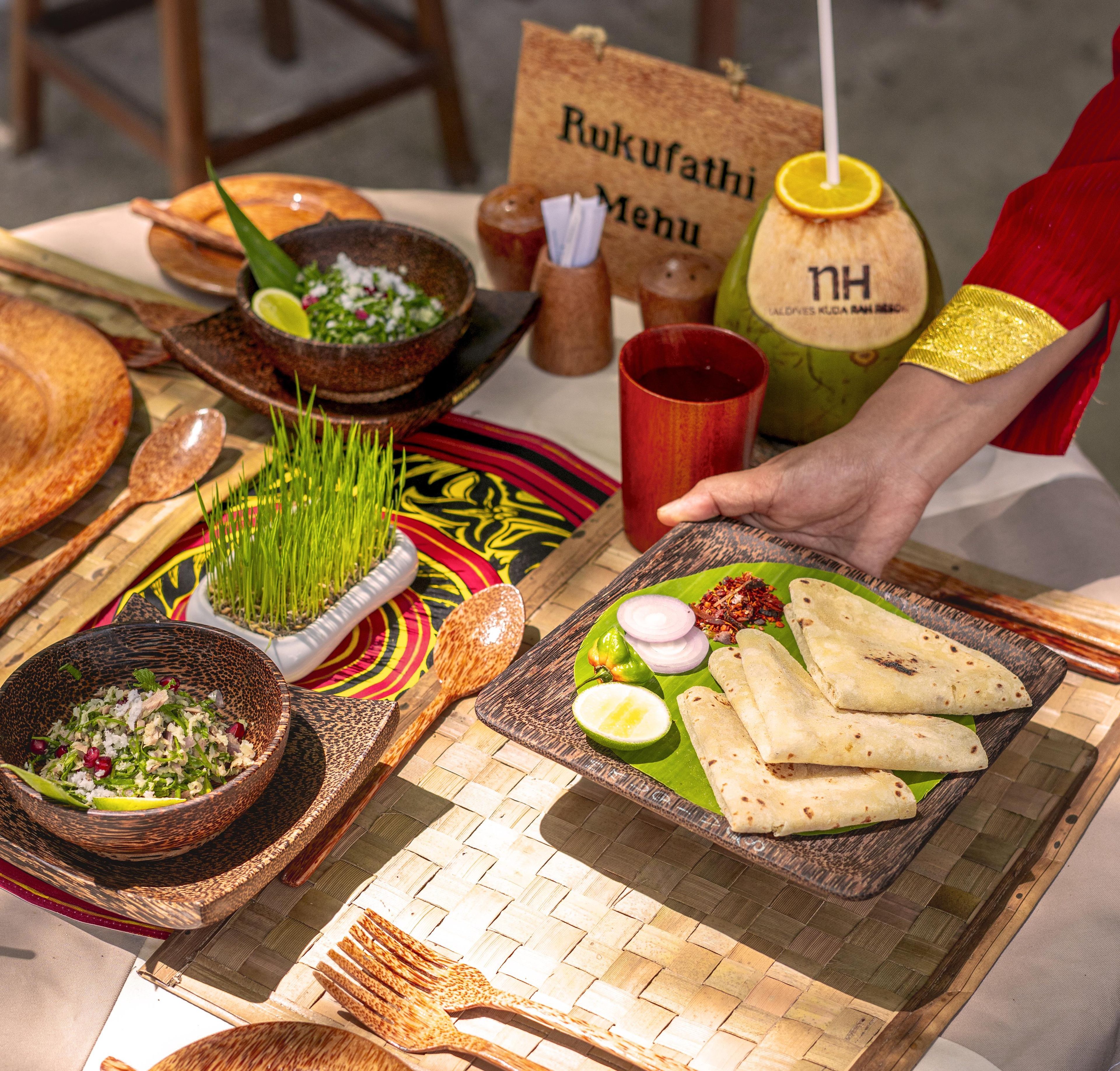 A table with various dishes, including a bowl of salad, a plate with flatbreads, and a red cup.