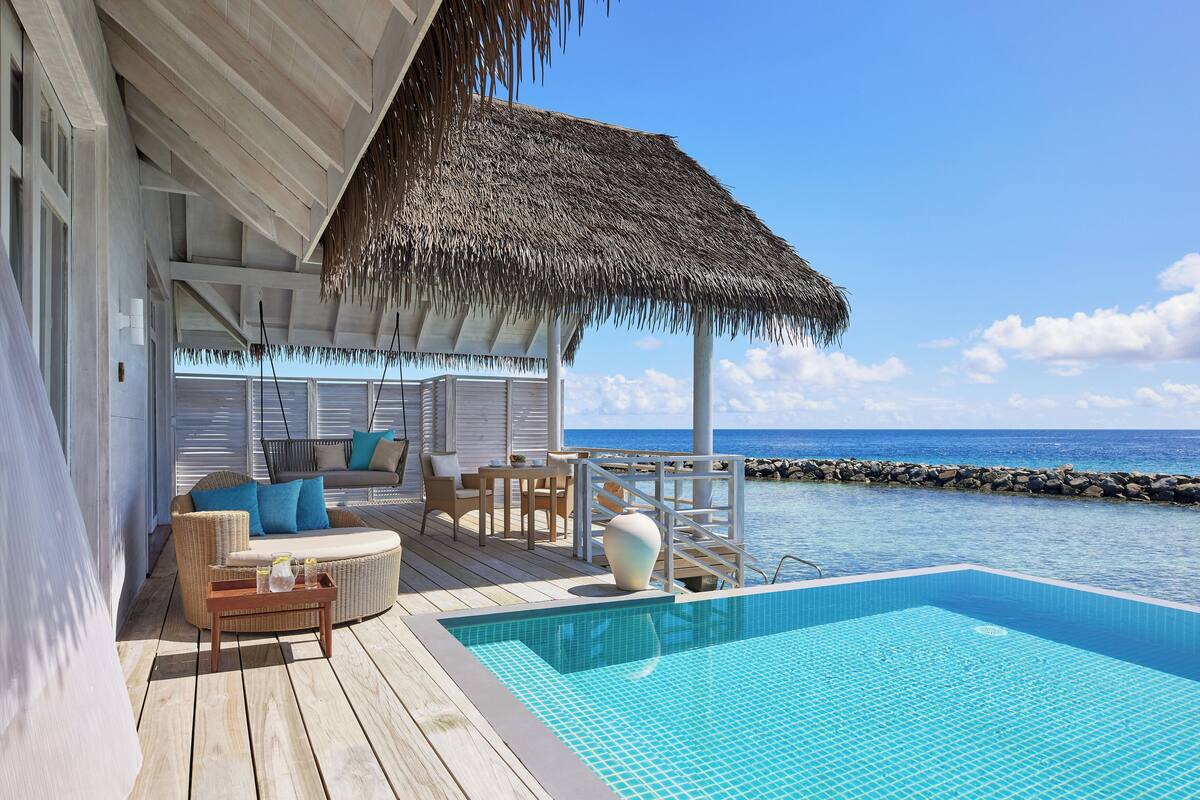 A wooden deck with a pool, lounge chairs, and a thatched roof structure overlooking the ocean.