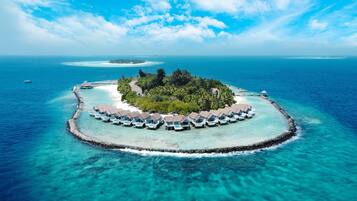 Un resort sobre el agua con alojamientos tipo bungalow, aguas turquesas cristalinas y una pequeña isla con exuberante vegetación.