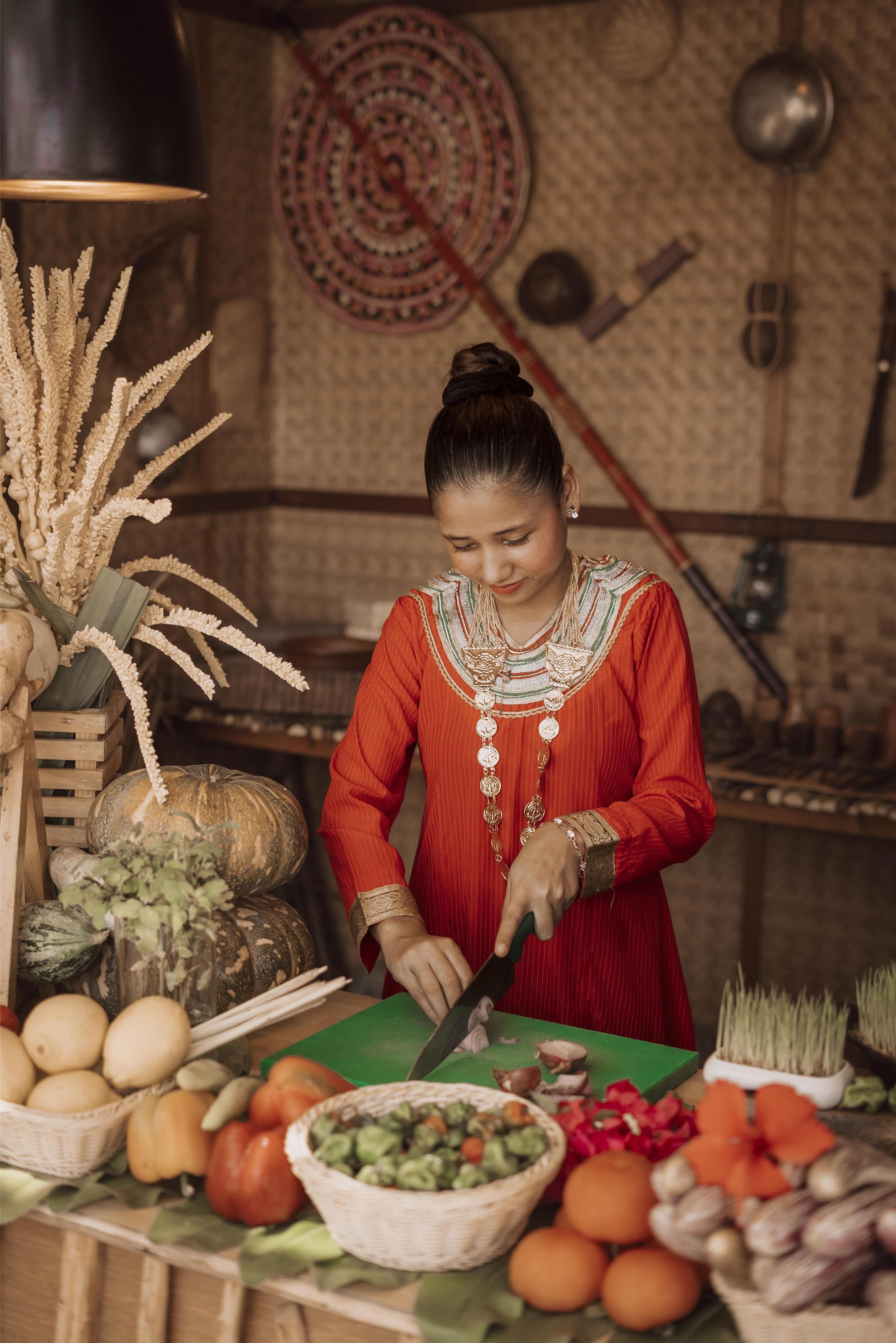 A person preparing food at a wooden table with various vegetables and a cutting board.