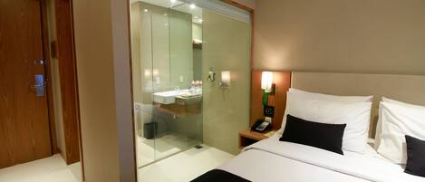Une chambre d’hôtel comprenant un lit, une table de chevet et une douche séparée par des parois en verre.
