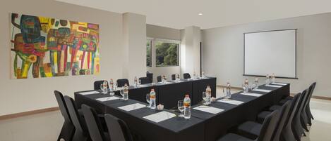 A conference room with a long table, chairs, a projector screen, and a painting on the wall.