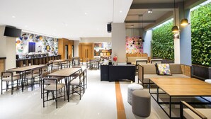 Un café moderno con mesas y sillas de madera, una zona de bar y una pared verde con un mural.
