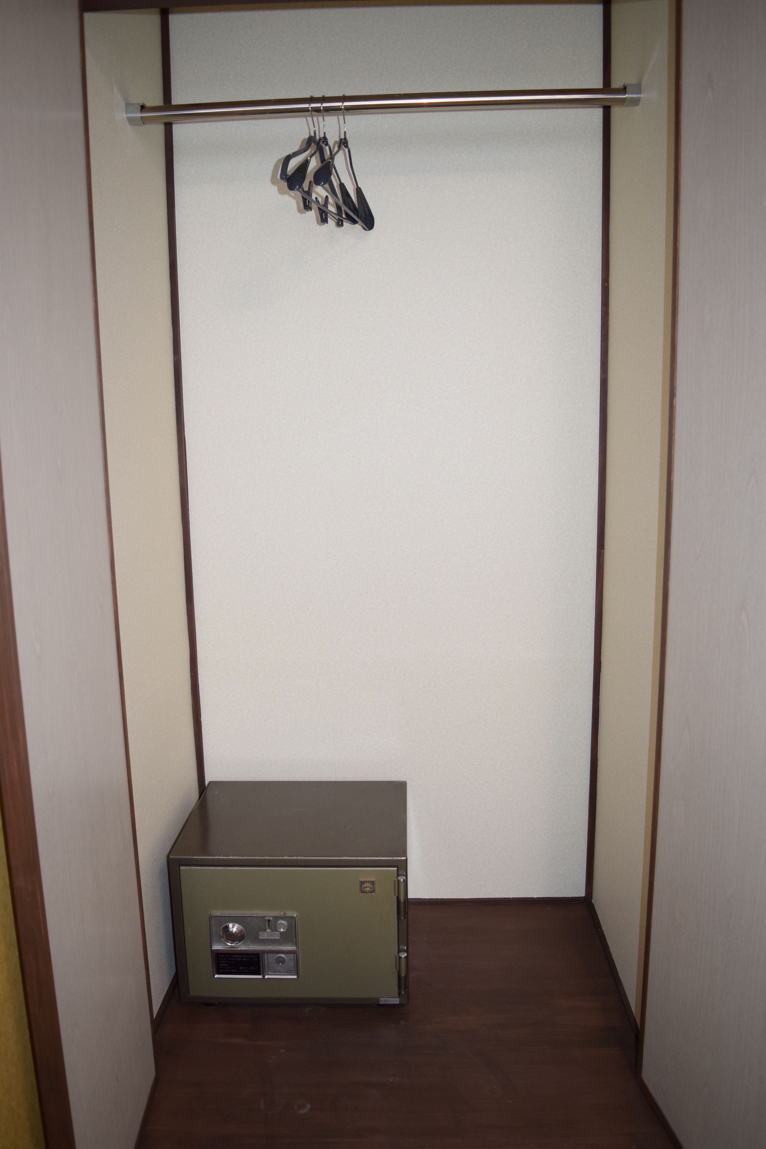 Un dressing avec une porte, un coffre-fort en métal, une tringle pour suspendre les vêtements et un plancher en bois.