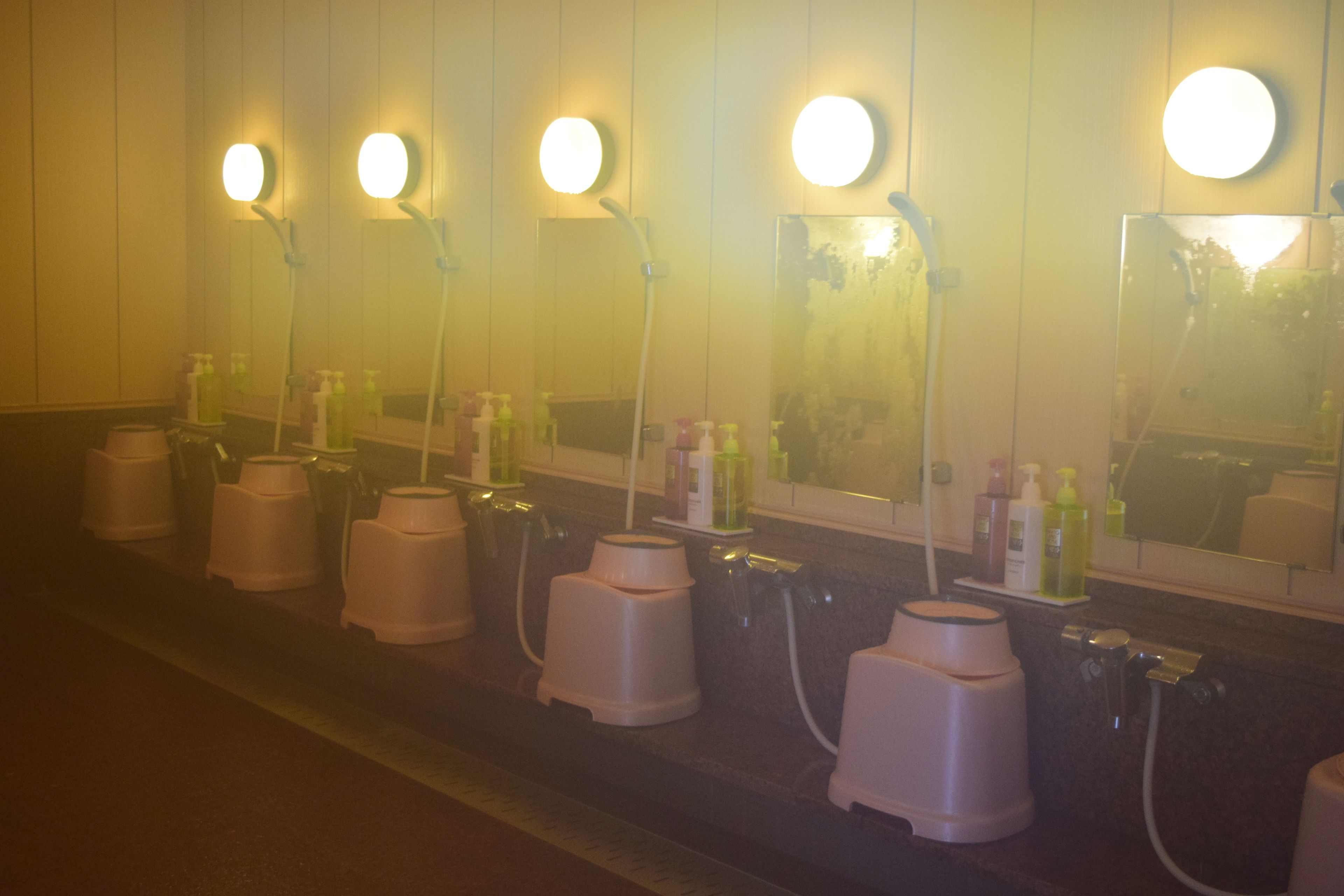 A row of sinks with mirrors and soap dispensers, each with a circular light above.