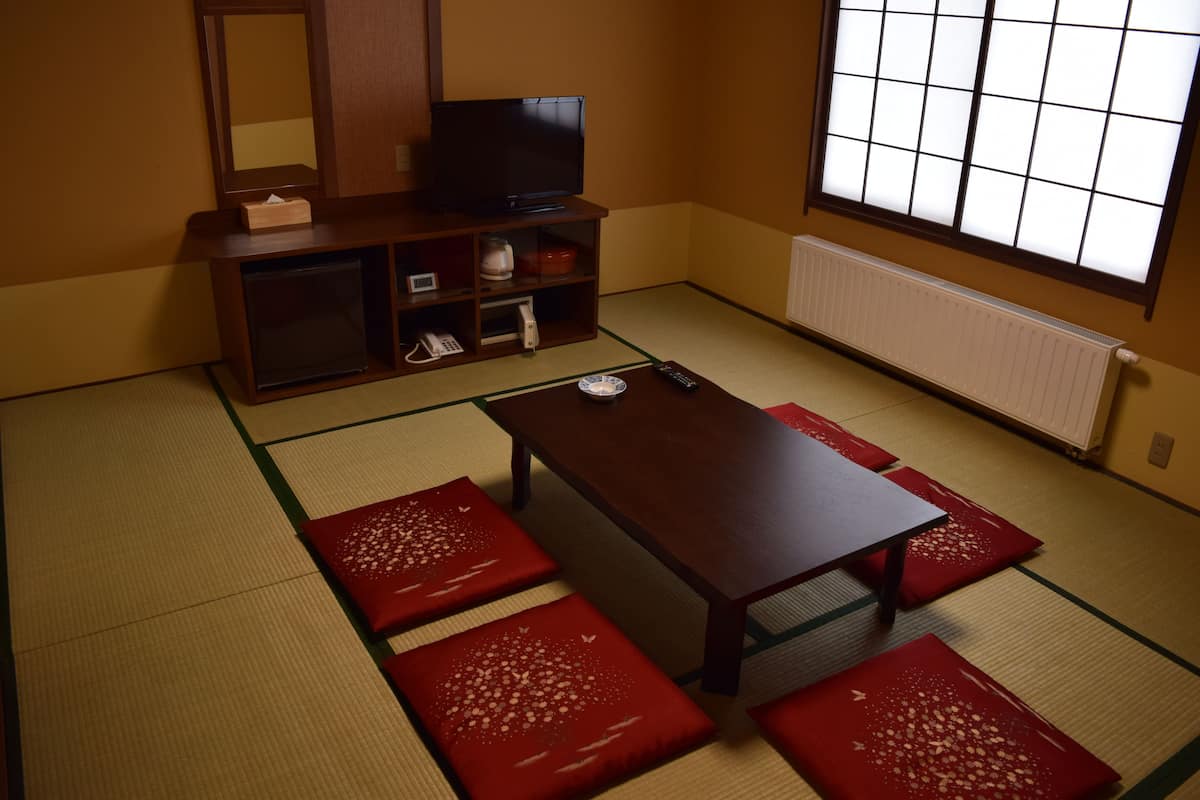 A traditional Japanese room with tatami flooring, a low wooden table, and red cushions.