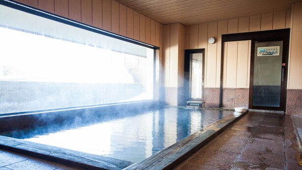 Un onsen japonés tradicional con un balneario de piedra, paredes de madera y suelo de baldosas.