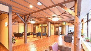 Un interior espacioso con piso de madera, un techo alto con vigas a la vista y una zona de estar con mobiliario de mimbre.