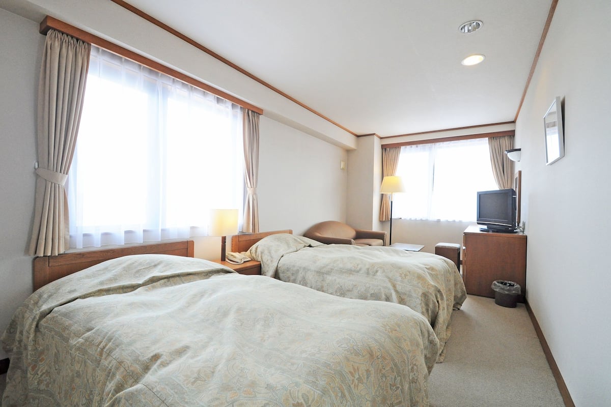 A hotel room with two beds, a television, a desk with a lamp, and a window with curtains.