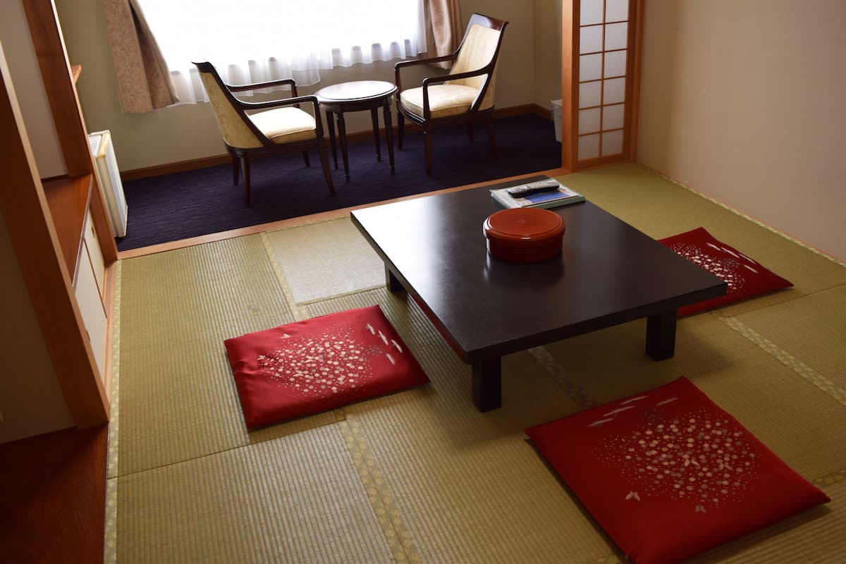 A traditional Japanese room with tatami flooring, a low table, and two chairs.