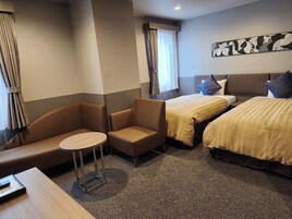 Una habitación de hotel con dos camas, una mesita, un sofá y una ventana con cortinas.