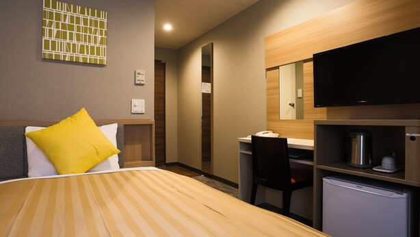 Habitación de hotel con cama, escritorio, silla, televisión y mini refrigerador.