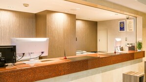 Zona de recepción de un hotel con mostrador de mármol, escritorio de recepción, computadora y cámara de seguridad instalada en la pared.