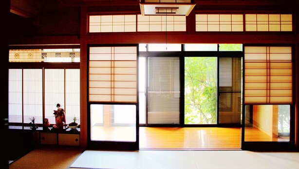 A traditional Japanese room with tatami flooring, sliding shoji doors, and a view of greenery outside.