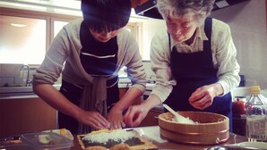 Two people preparing food in a kitchen with wooden cabinets and a window.