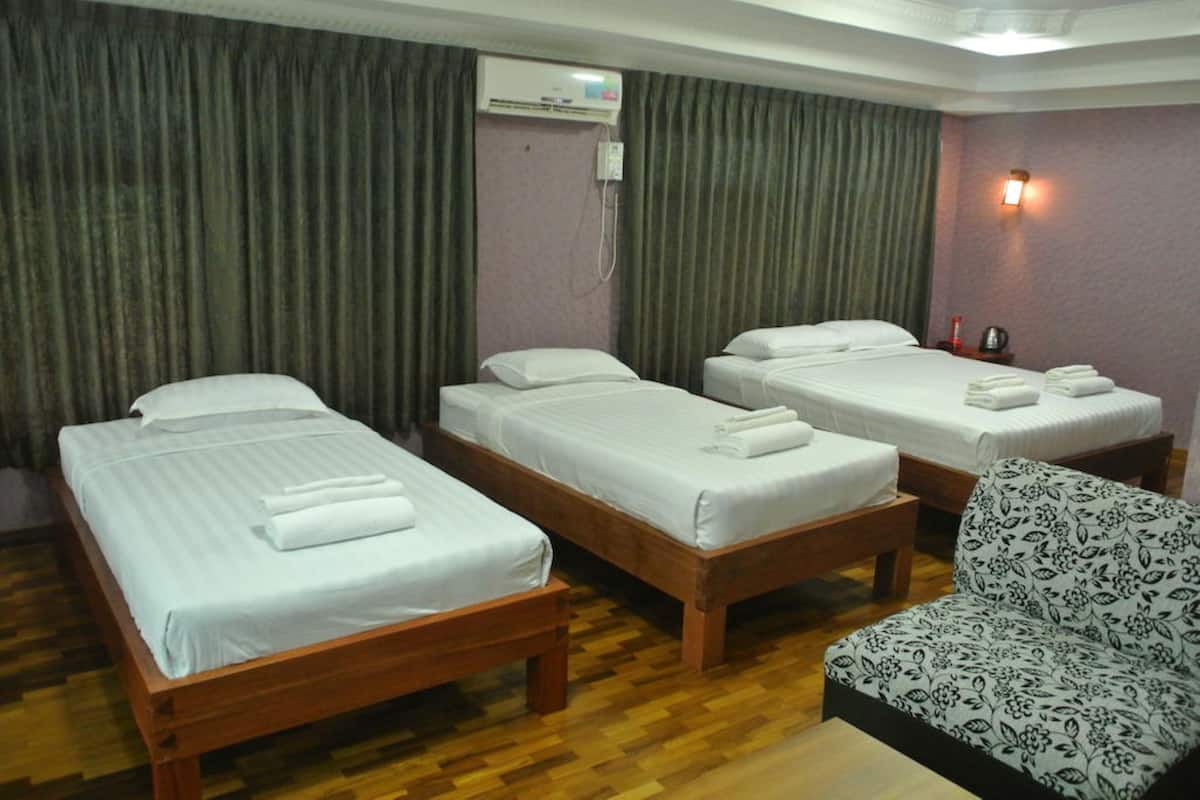 Una habitación de hotel con tres camas de madera, un sillón estampado con motivos florales y un equipo de aire acondicionado en la pared.