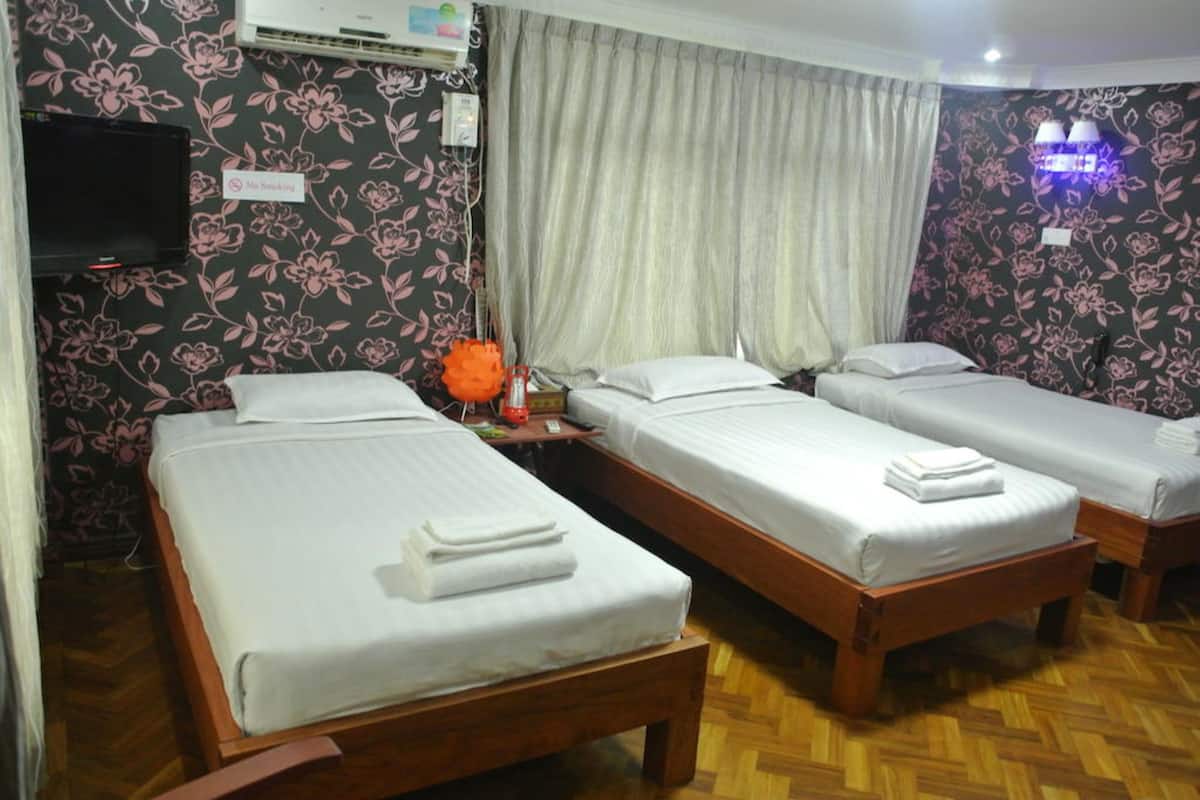 Habitación de hotel con tres camas individuales, televisión, un cartel de 'No Fumar' y papel tapiz floral.
