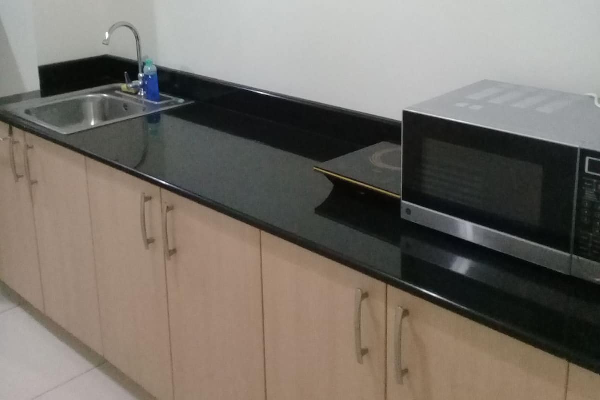 A kitchen with a black countertop, a stainless steel sink, a microwave, and beige cabinets.