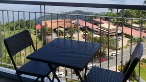 A balcony with two chairs and a table, overlooking a coastal area with buildings and a road. - The Concierge at Wind Residences Tagaytay (Tagaytay)