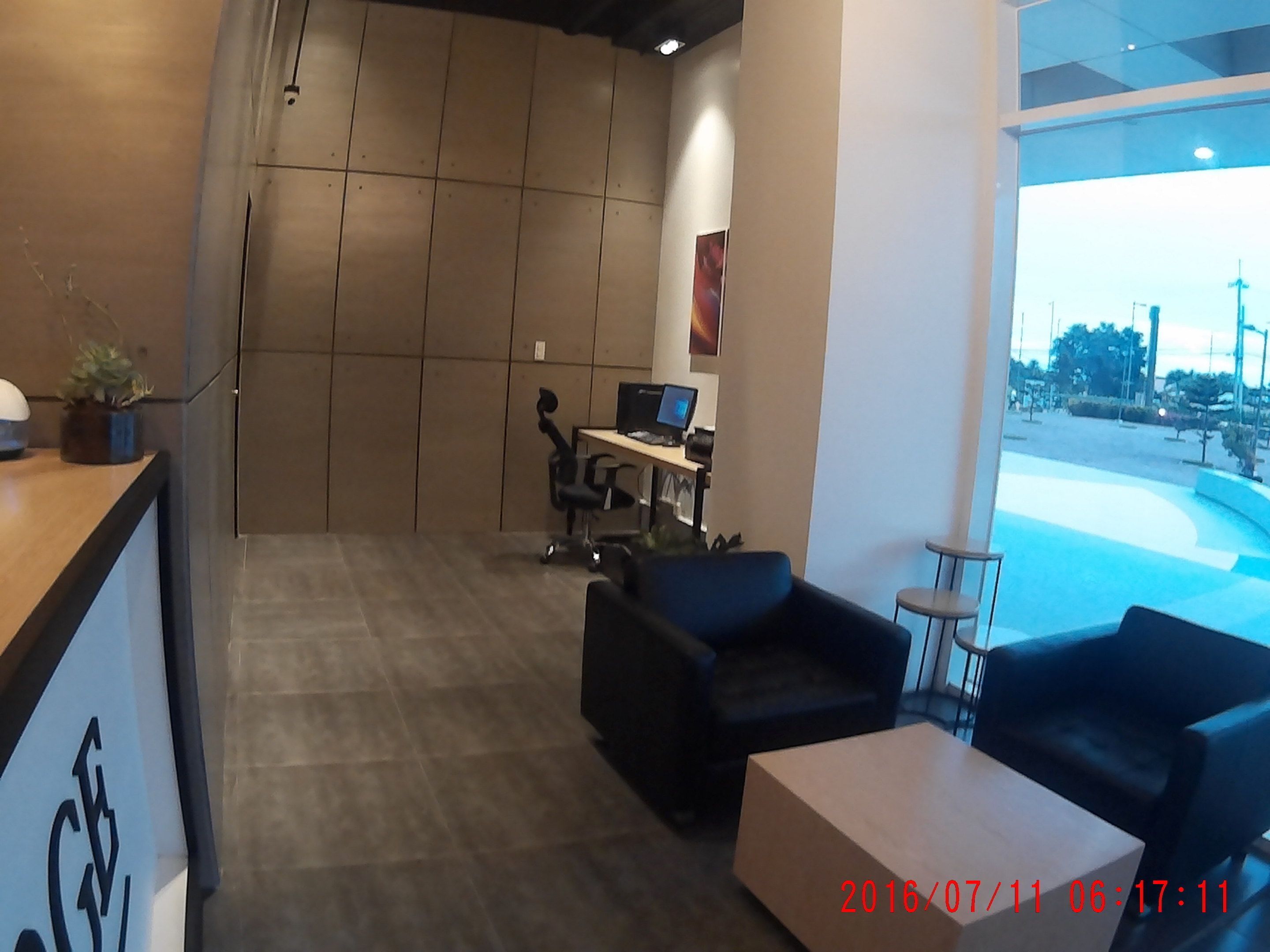 A modern office space with a reception desk, two black office chairs, a small table, and a computer desk with a monitor.