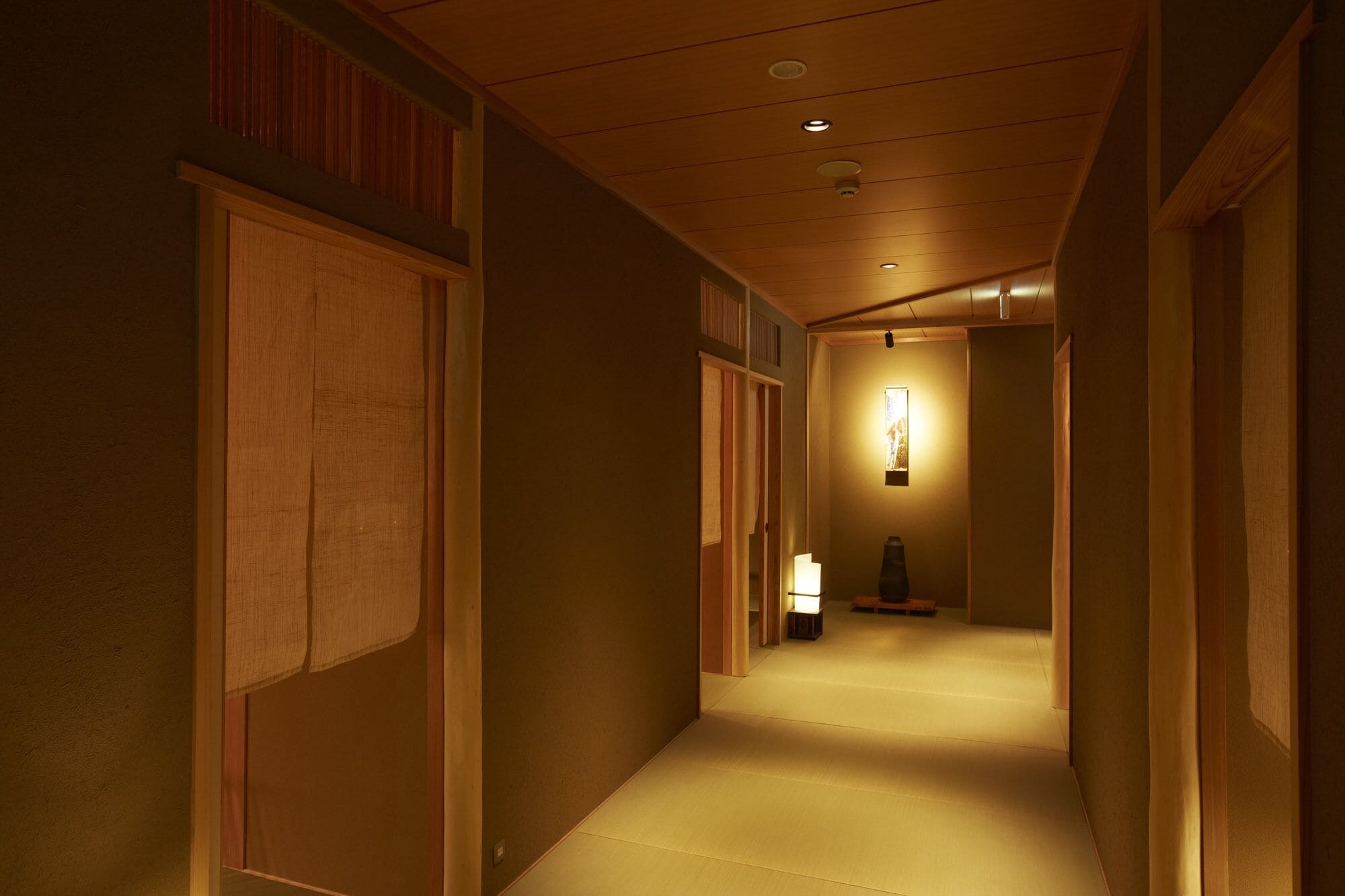 A narrow hallway with wooden doors and a soft light source at the end.