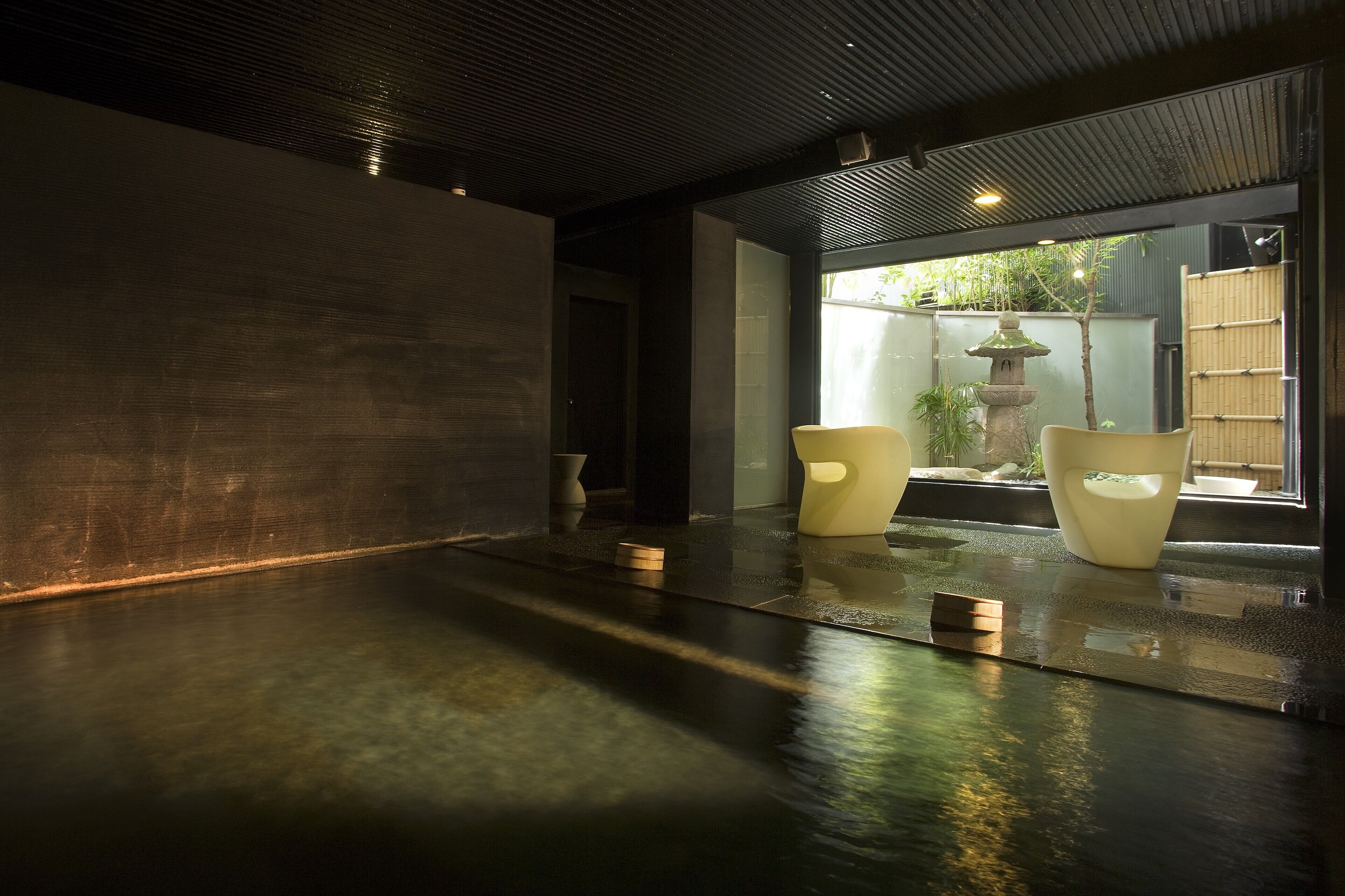 A modern interior with a wet floor, two chairs, and a stone lantern by a window.
