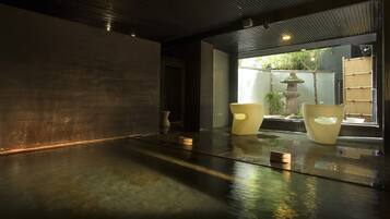 A modern interior with a wet floor, two chairs, and a stone lantern by a window.