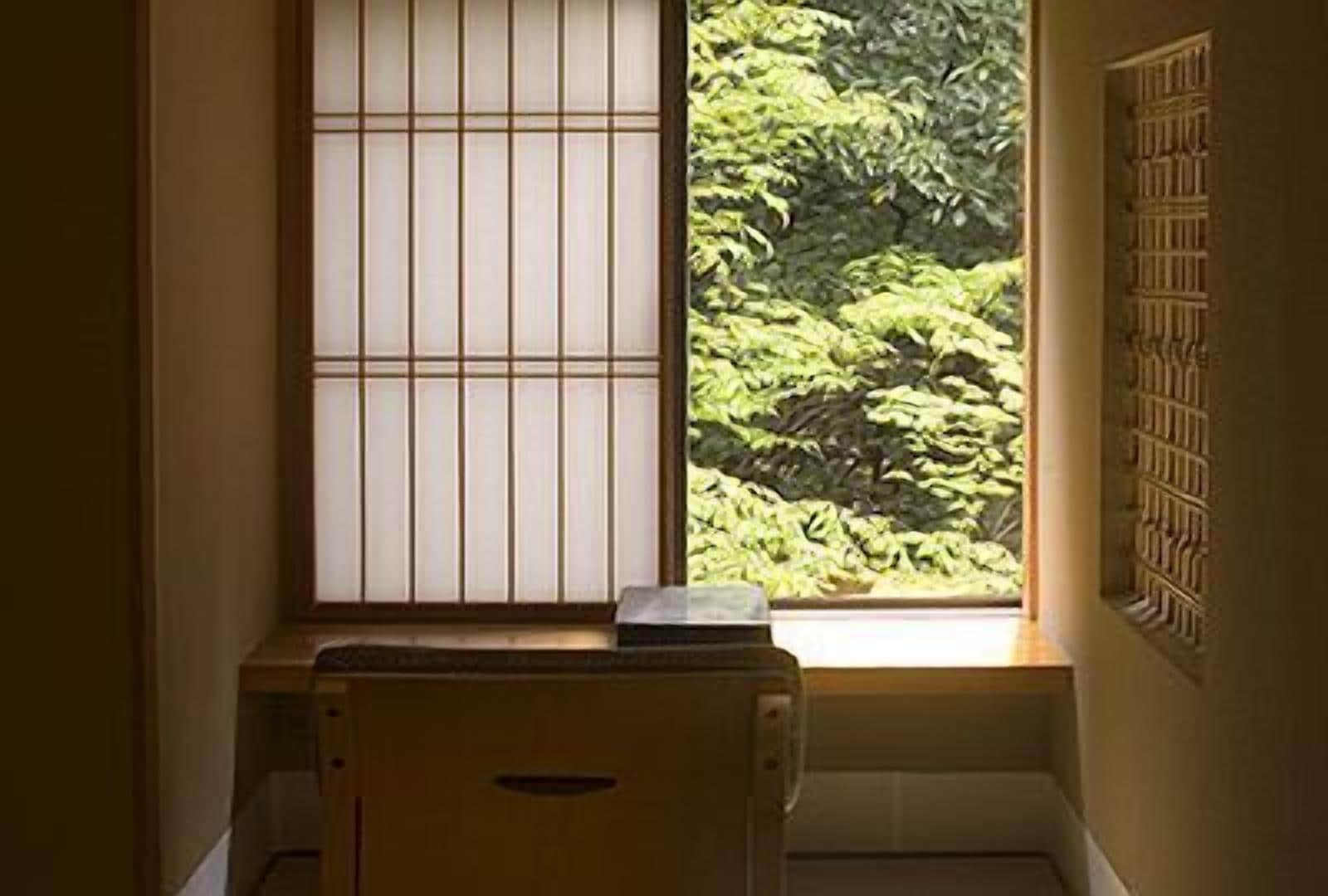 Una habitación con una puerta shoji japonesa tradicional, un pequeño escritorio de madera y vistas a abundante follaje exterior.