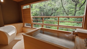 Une salle de bain moderne avec une grande baignoire, un plancher en bois et une vue sur une forêt, visible à travers une grande fenêtre.