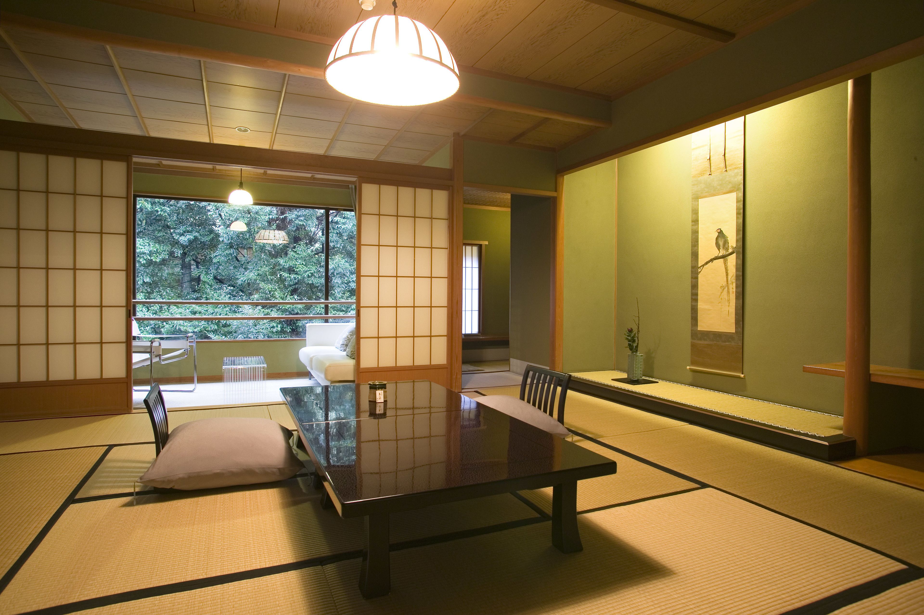 A traditional Japanese room with tatami flooring, a low table, and a sliding door leading to a balcony with a view of trees.