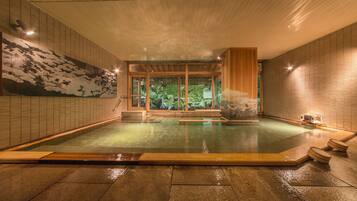 Un onsen japonés tradicional con interior de madera, suelo de piedra y vistas a un paisaje natural a través de puertas correderas.