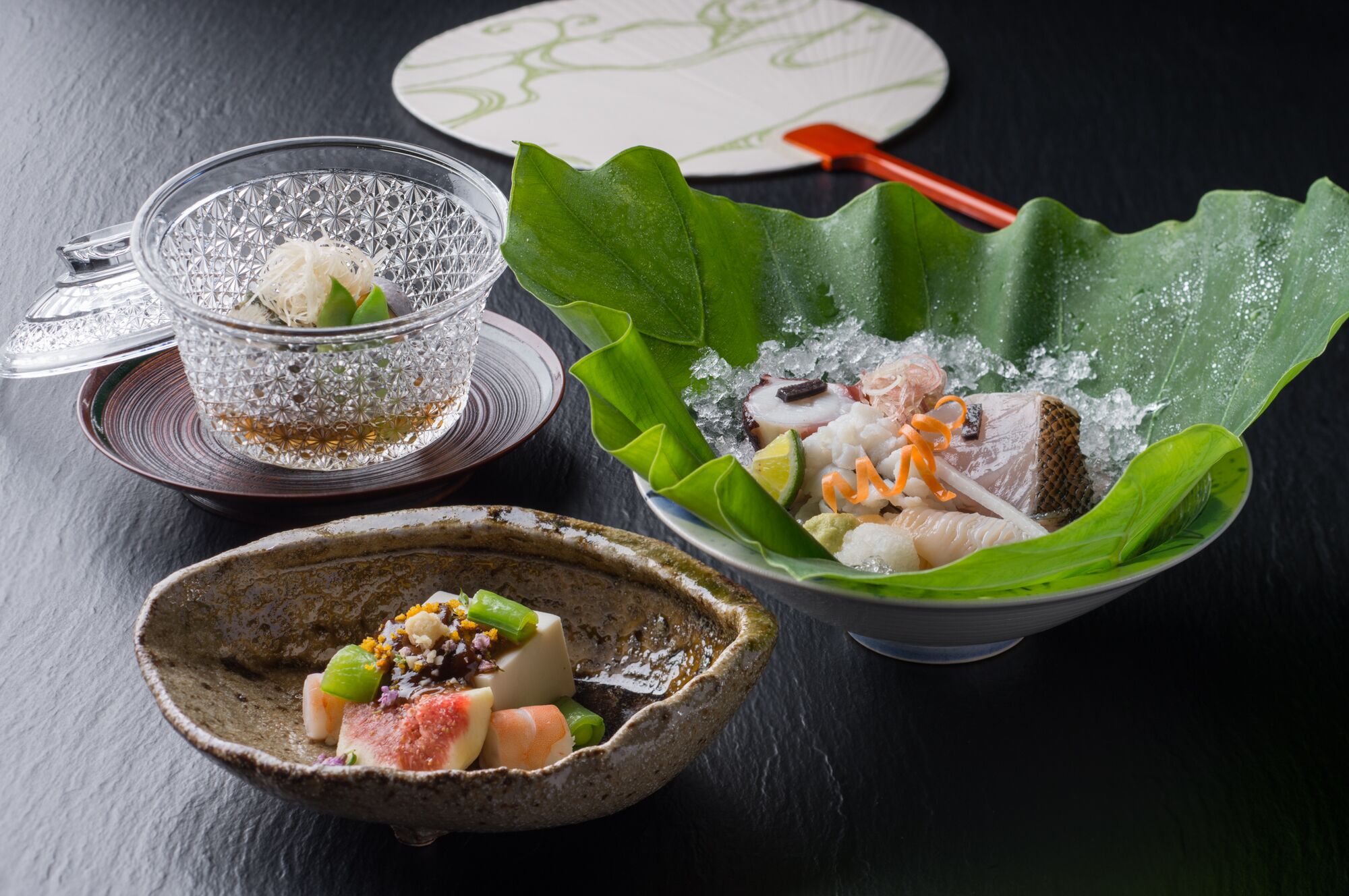 A table setting with a glass bowl containing a seafood dish, a ceramic bowl with a seafood dish, and a plate with a green leaf.