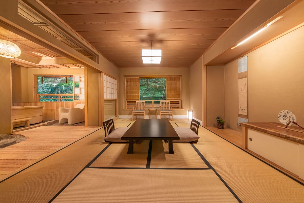 A traditional Japanese-style room with tatami flooring, a low table with cushions, and sliding doors leading to a garden view.