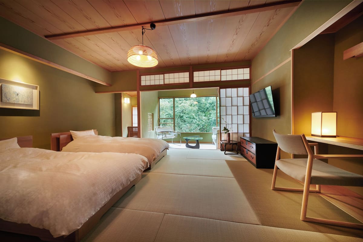 A traditional Japanese-style room with tatami flooring, a bed, a desk, and a TV.