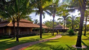 Um resort com construções de telhado de palha, um gramado bem cuidado e palmeiras.