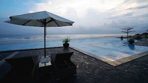 Uma área na piscina com vista para o oceano, uma espreguiçadeira, uma mesa e um guarda-sol.