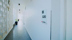 A hallway with a sign indicating room number 120, a modern design with geometric wall patterns, and potted plants along the corridor.