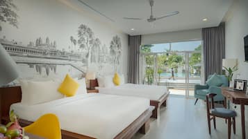 A hotel room with two beds, a desk, a chair, a ceiling fan, and a large window with a view of a pool and greenery.