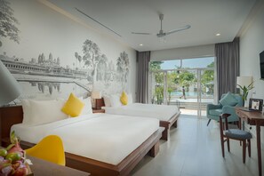 Une chambre d’hôtel avec deux lits, un bureau, une chaise, un ventilateur de plafond et une grande fenêtre donnant sur une piscine et un espace verdoyant.