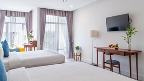 A hotel room with two beds, a desk, a chair, a TV, and a ceiling fan.