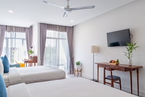 A hotel room with two beds, a desk, a chair, a TV, and a ceiling fan.