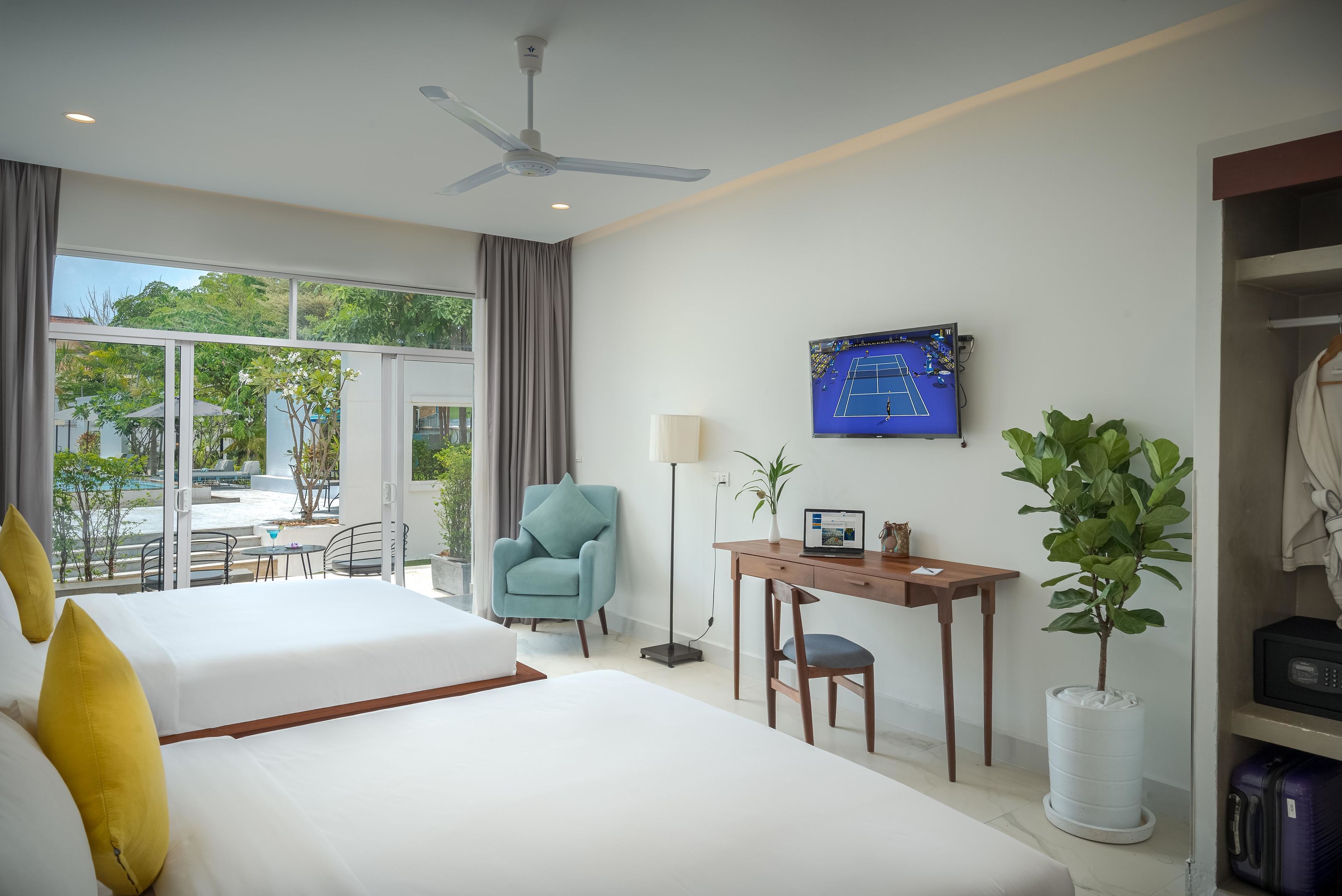 A hotel room with two beds, a desk, a chair, a TV, and a view of the outdoors.