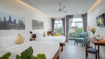 A hotel room with two beds, a desk, a chair, a TV, and a balcony with a view of a temple and trees.