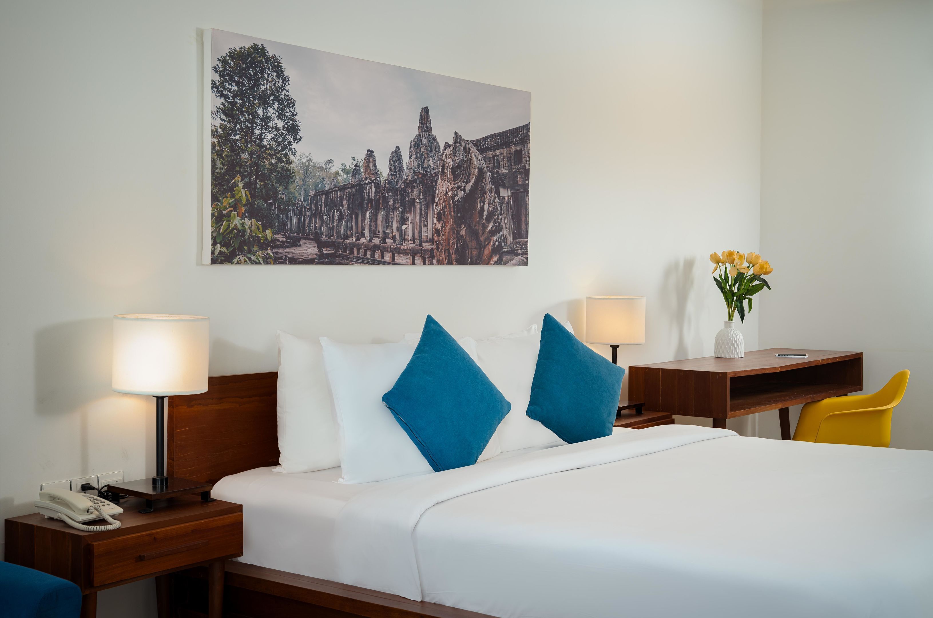 Een hotelkamer met een bed, twee nachtkastjes, een bureau, een stoel en een schilderij aan de muur.