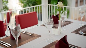 A dining table set with wine glasses, a vase with a flower, and red napkins. - Elysium Suite (Siem Reap)